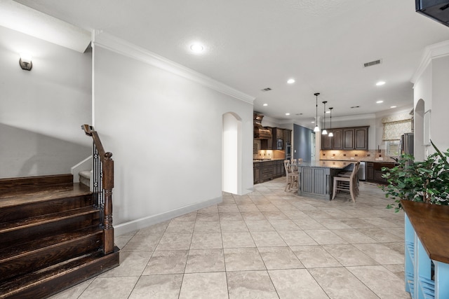 interior space with backsplash, dark brown cabinets, a kitchen breakfast bar, a center island, and ornamental molding