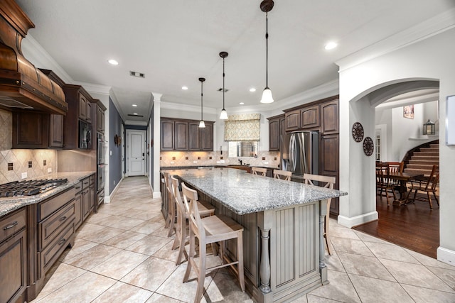 kitchen with a breakfast bar area, appliances with stainless steel finishes, dark brown cabinets, light stone countertops, and a kitchen island