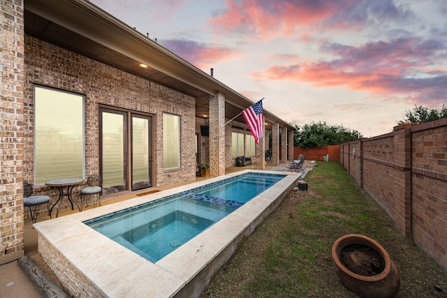 pool at dusk with an in ground hot tub and a patio area