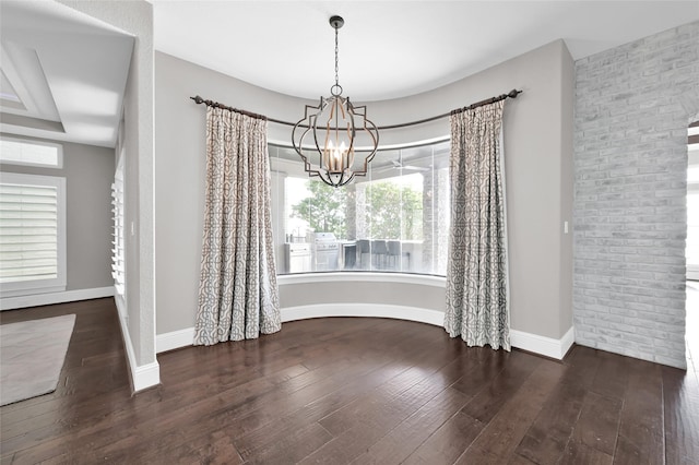 unfurnished dining area featuring hardwood / wood-style flooring, brick wall, baseboards, and an inviting chandelier