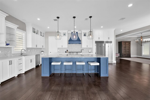 kitchen with stainless steel appliances, premium range hood, dark wood-style flooring, a breakfast bar, and white cabinets