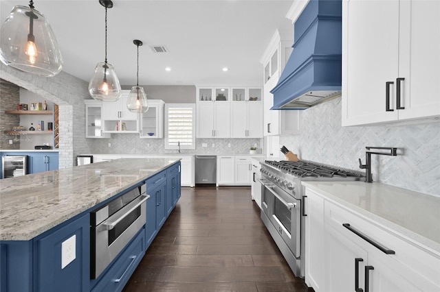 kitchen with blue cabinets, visible vents, appliances with stainless steel finishes, custom exhaust hood, and open shelves