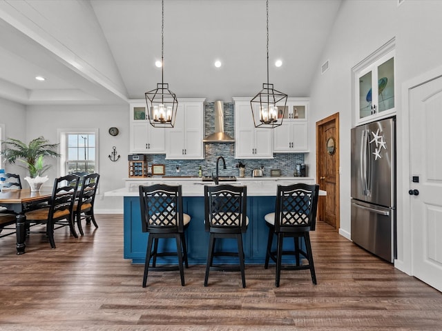 kitchen featuring pendant lighting, stainless steel refrigerator, white cabinets, and a center island with sink