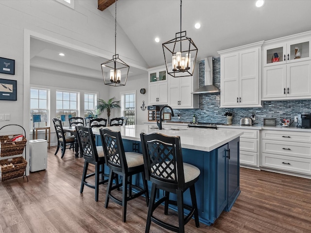 kitchen featuring pendant lighting, sink, white cabinets, a kitchen island with sink, and wall chimney range hood