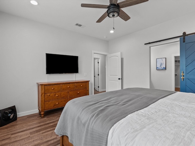 bedroom featuring dark hardwood / wood-style flooring, a barn door, and ceiling fan