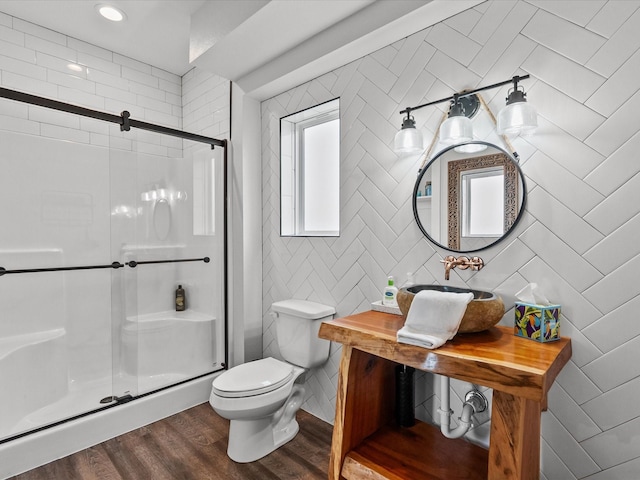 bathroom featuring toilet, sink, tile walls, a shower with door, and hardwood / wood-style flooring