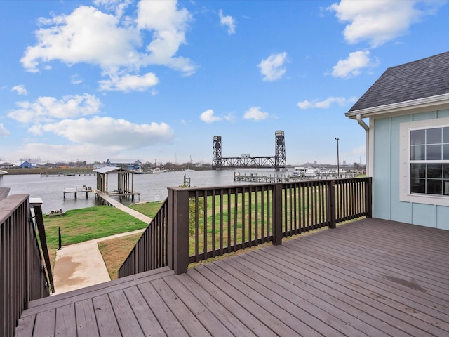 wooden terrace with a water view, a dock, and a lawn