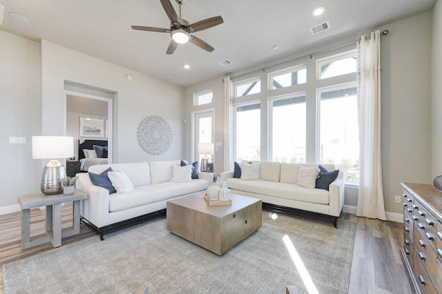 living room featuring baseboards, a ceiling fan, visible vents, and light wood-type flooring