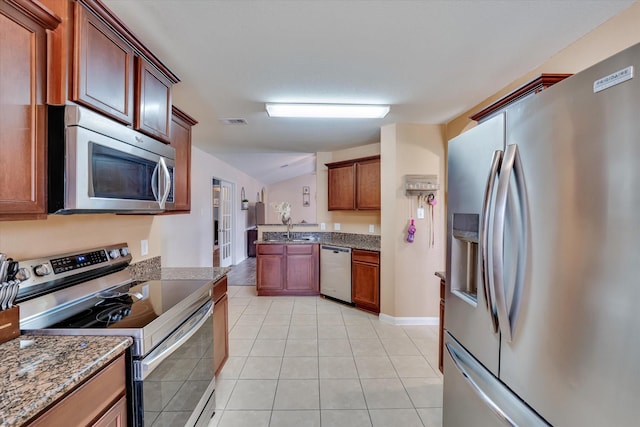 kitchen with sink, vaulted ceiling, dark stone countertops, light tile patterned floors, and appliances with stainless steel finishes