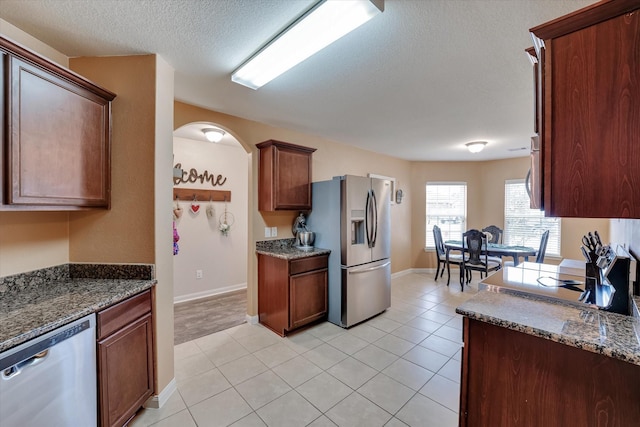 kitchen featuring dark stone countertops, light tile patterned floors, stainless steel appliances, and a textured ceiling