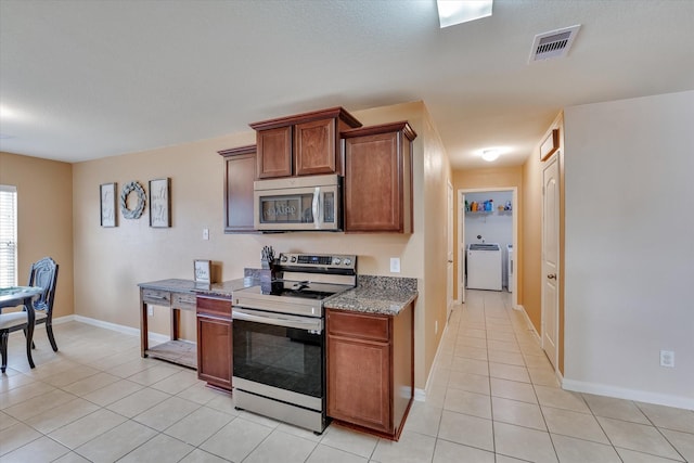 kitchen with dark stone countertops, light tile patterned floors, washer / dryer, and appliances with stainless steel finishes