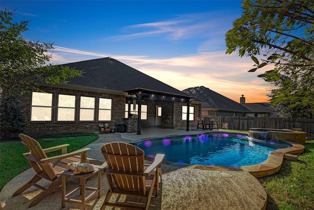 pool at dusk with a patio area and an in ground hot tub