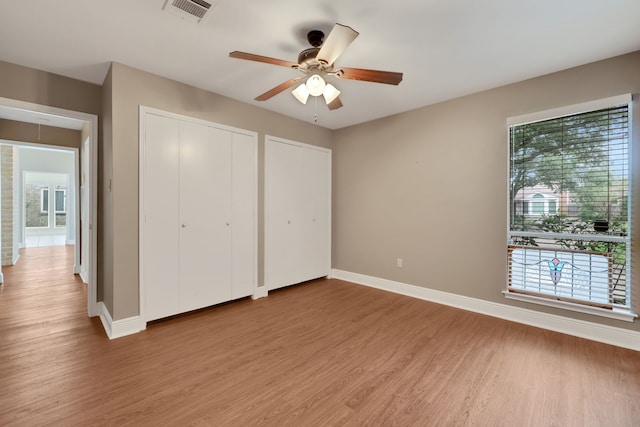 unfurnished bedroom featuring hardwood / wood-style floors, multiple closets, and ceiling fan