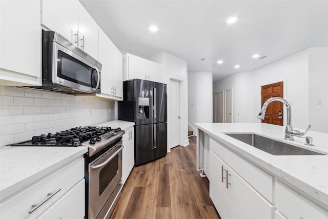 kitchen with sink, appliances with stainless steel finishes, white cabinetry, backsplash, and dark hardwood / wood-style flooring