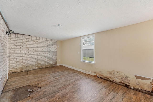 empty room featuring hardwood / wood-style floors, a textured ceiling, and brick wall