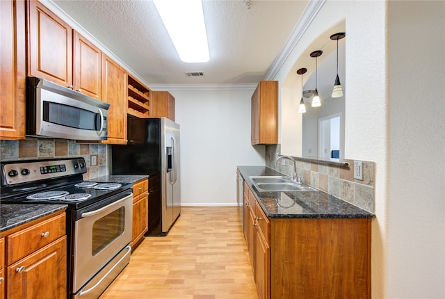 kitchen featuring pendant lighting, sink, ornamental molding, stainless steel appliances, and light wood-type flooring