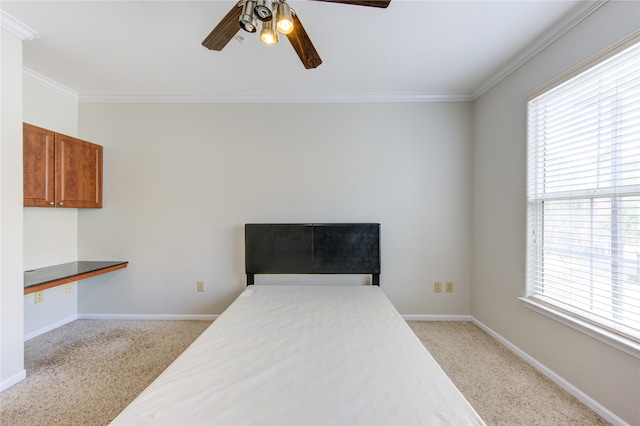 bedroom with light carpet, crown molding, built in desk, and ceiling fan