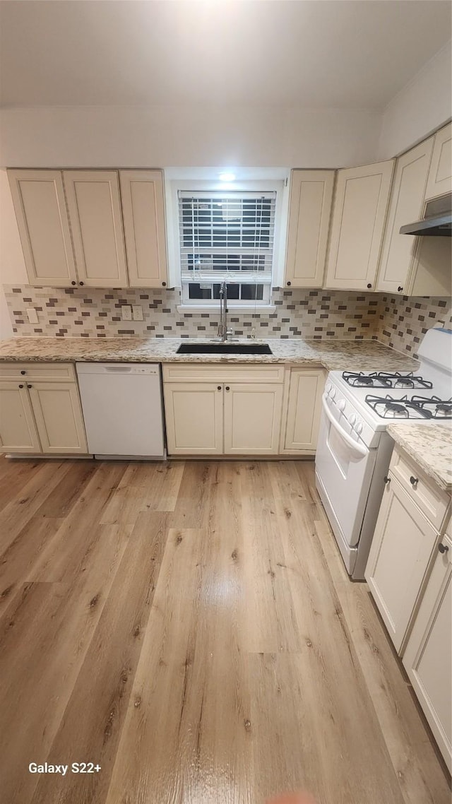 kitchen featuring white appliances, decorative backsplash, light wood-type flooring, under cabinet range hood, and a sink