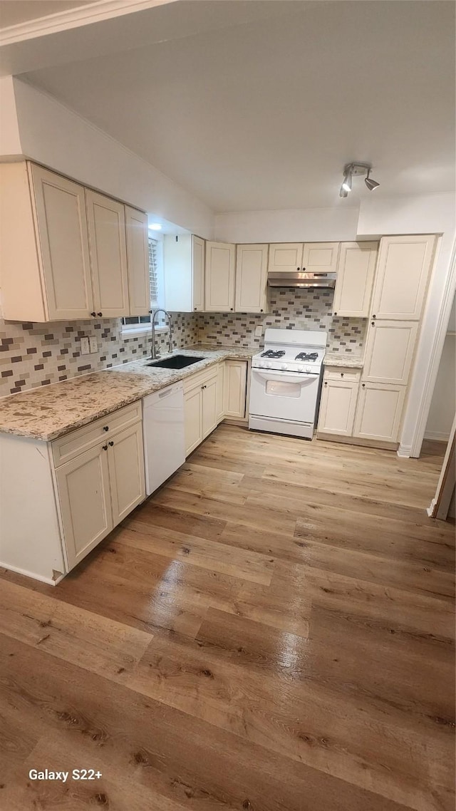 kitchen featuring light wood finished floors, decorative backsplash, a sink, white appliances, and under cabinet range hood