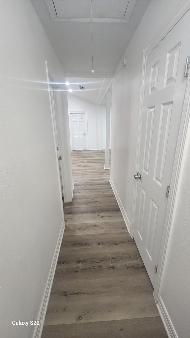 hall featuring attic access, vaulted ceiling, baseboards, and wood finished floors