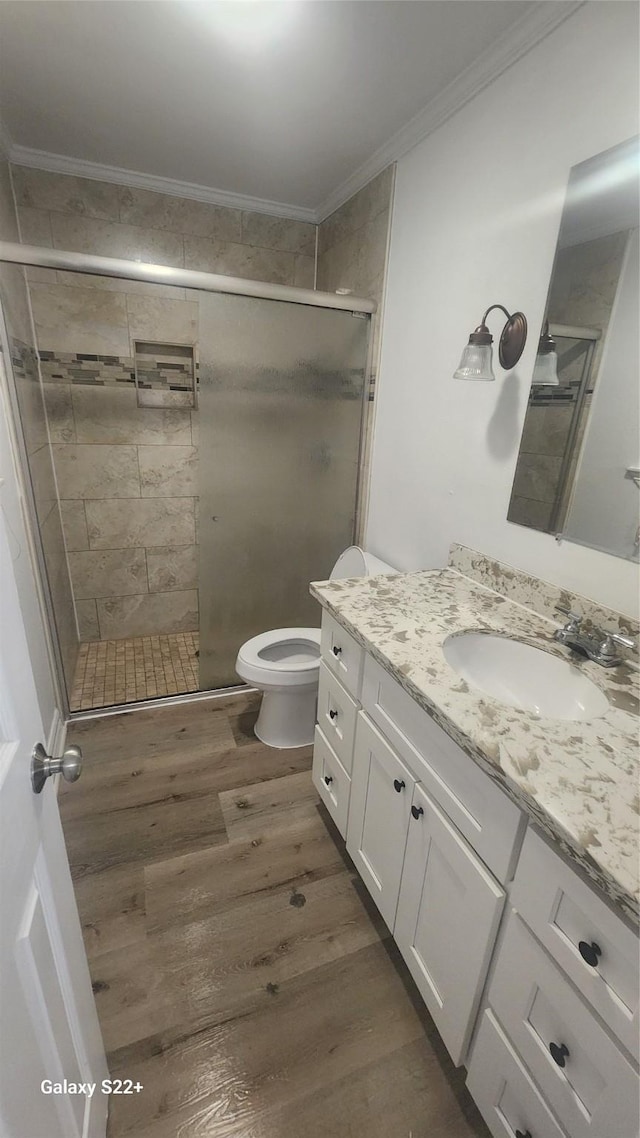 full bathroom with crown molding, toilet, vanity, a shower stall, and wood finished floors