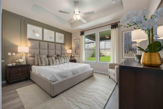 bedroom featuring a raised ceiling, ceiling fan, and light hardwood / wood-style flooring