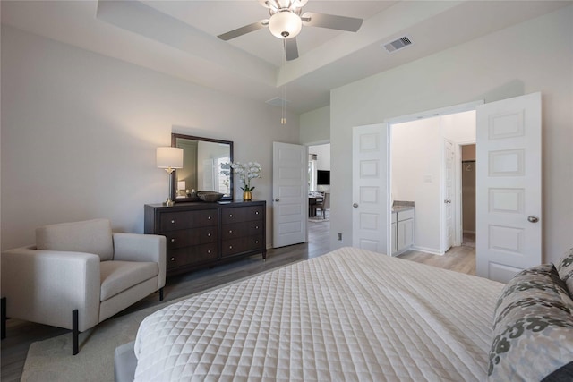 bedroom with ceiling fan, a raised ceiling, and light hardwood / wood-style floors