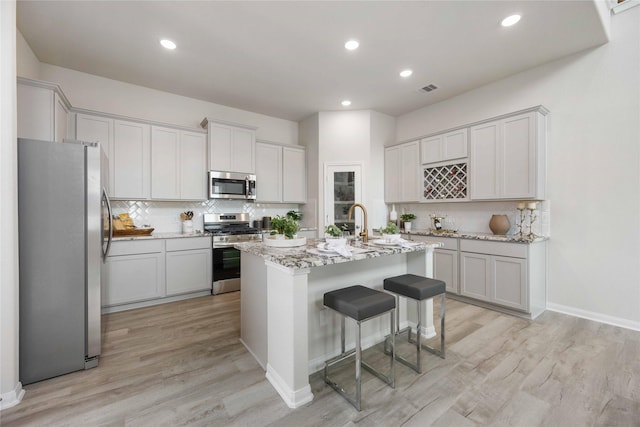 kitchen with appliances with stainless steel finishes, a kitchen island with sink, white cabinetry, light stone countertops, and a kitchen bar