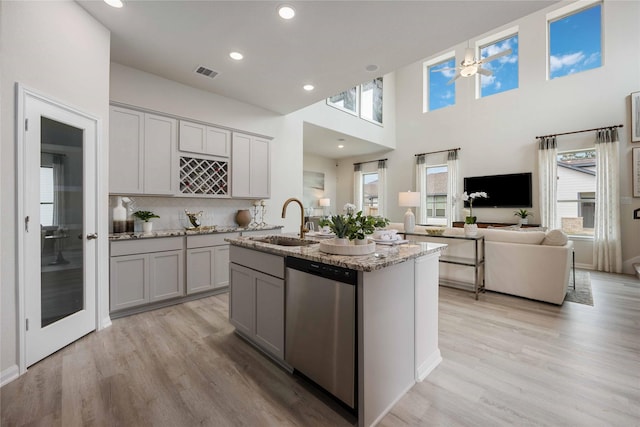 kitchen with gray cabinets, sink, a kitchen island with sink, stainless steel dishwasher, and light stone countertops