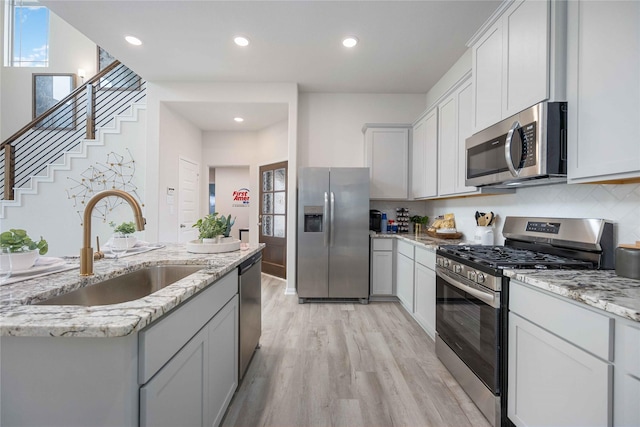 kitchen featuring sink, light hardwood / wood-style flooring, appliances with stainless steel finishes, white cabinetry, and backsplash