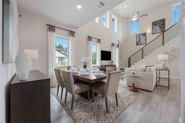 dining room with a high ceiling, ceiling fan, and light wood-type flooring