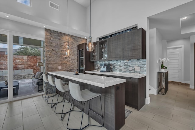 kitchen featuring dark brown cabinetry, tasteful backsplash, hanging light fixtures, a towering ceiling, and a large island