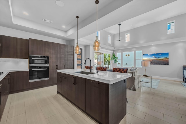 kitchen featuring decorative light fixtures, sink, a high ceiling, double wall oven, and a center island with sink