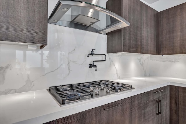 kitchen with tasteful backsplash, dark brown cabinets, range hood, and stainless steel gas cooktop