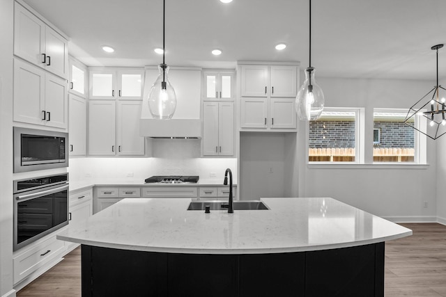 kitchen with white cabinetry, appliances with stainless steel finishes, decorative light fixtures, and an island with sink