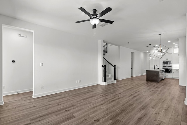 unfurnished living room featuring sink, ceiling fan with notable chandelier, and dark wood-type flooring