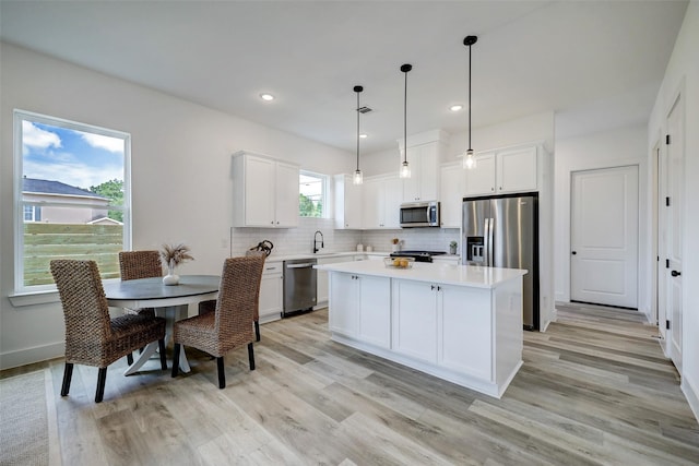 kitchen featuring a kitchen island, white cabinetry, sink, hanging light fixtures, and stainless steel appliances