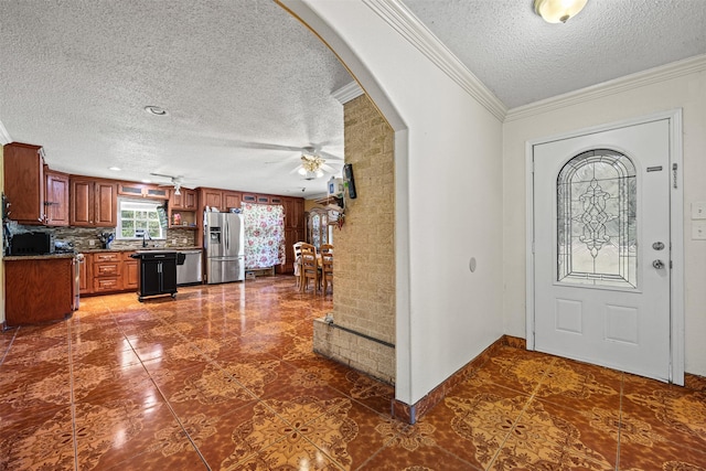 tiled entryway with ceiling fan, ornamental molding, and a textured ceiling