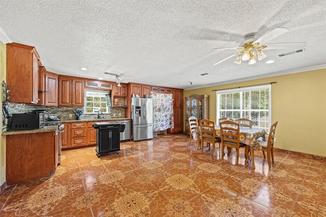 kitchen with light stone counters, ornamental molding, appliances with stainless steel finishes, ceiling fan, and backsplash