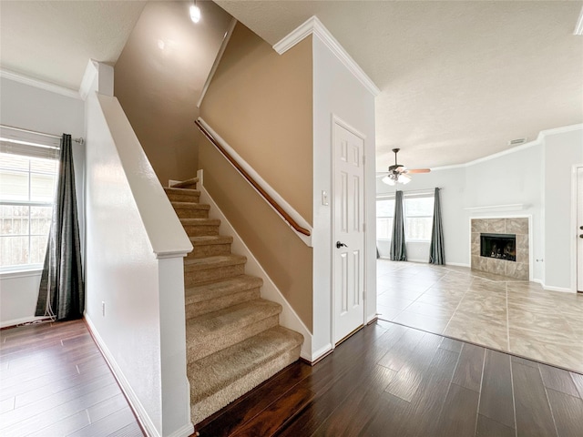stairway with hardwood / wood-style flooring, ceiling fan, crown molding, and a tile fireplace