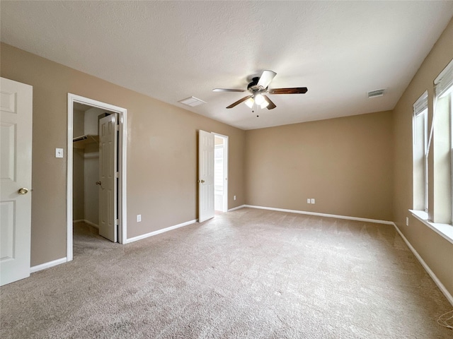unfurnished bedroom with a spacious closet, light carpet, a textured ceiling, and ceiling fan