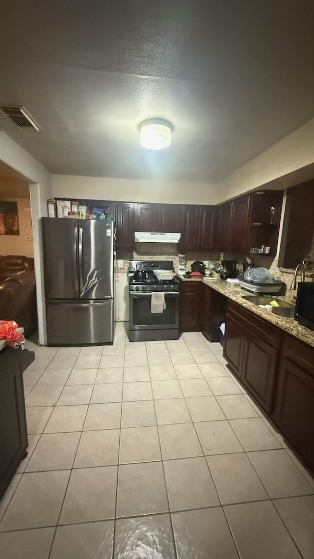 kitchen featuring light tile patterned flooring, under cabinet range hood, stainless steel appliances, visible vents, and light stone countertops