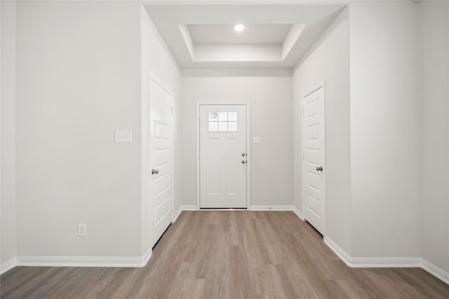 entryway with a tray ceiling, baseboards, and wood finished floors