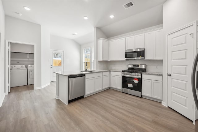 kitchen with a sink, visible vents, vaulted ceiling, appliances with stainless steel finishes, and independent washer and dryer