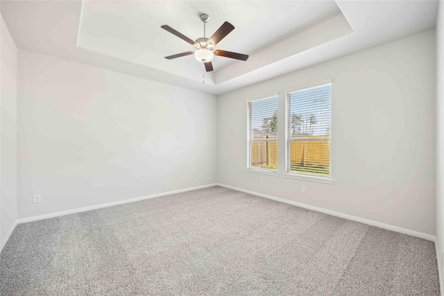 carpeted spare room with a tray ceiling, ceiling fan, and baseboards