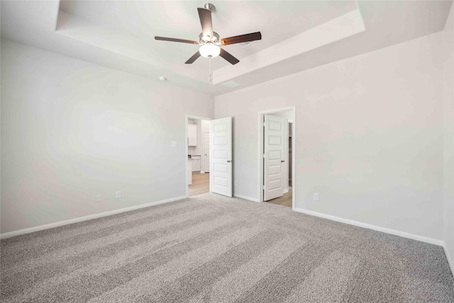 unfurnished bedroom featuring visible vents, a ceiling fan, baseboards, a tray ceiling, and carpet