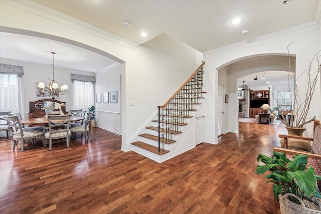 foyer entrance with arched walkways, stairway, wood finished floors, and an inviting chandelier