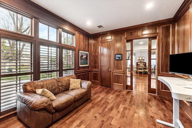 living area with wood walls, wood finished floors, visible vents, ornamental molding, and an inviting chandelier