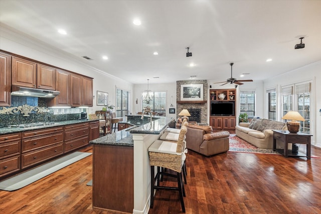 kitchen with visible vents, a kitchen breakfast bar, dark wood-style flooring, crown molding, and under cabinet range hood