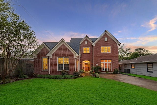 view of front of home featuring central air condition unit, brick siding, fence, a yard, and driveway